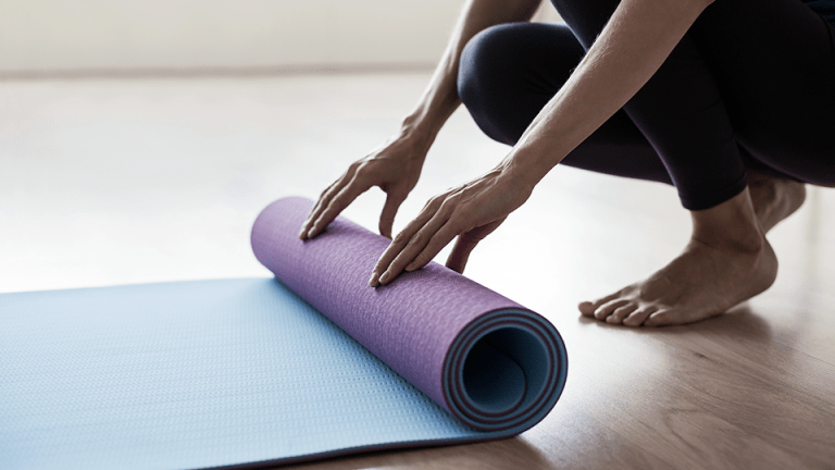 Personne déroulant un tapis de yoga sur le sol
